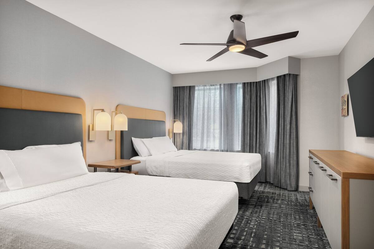 A hotel room with two beds, a ceiling fan, a desk, and a TV.