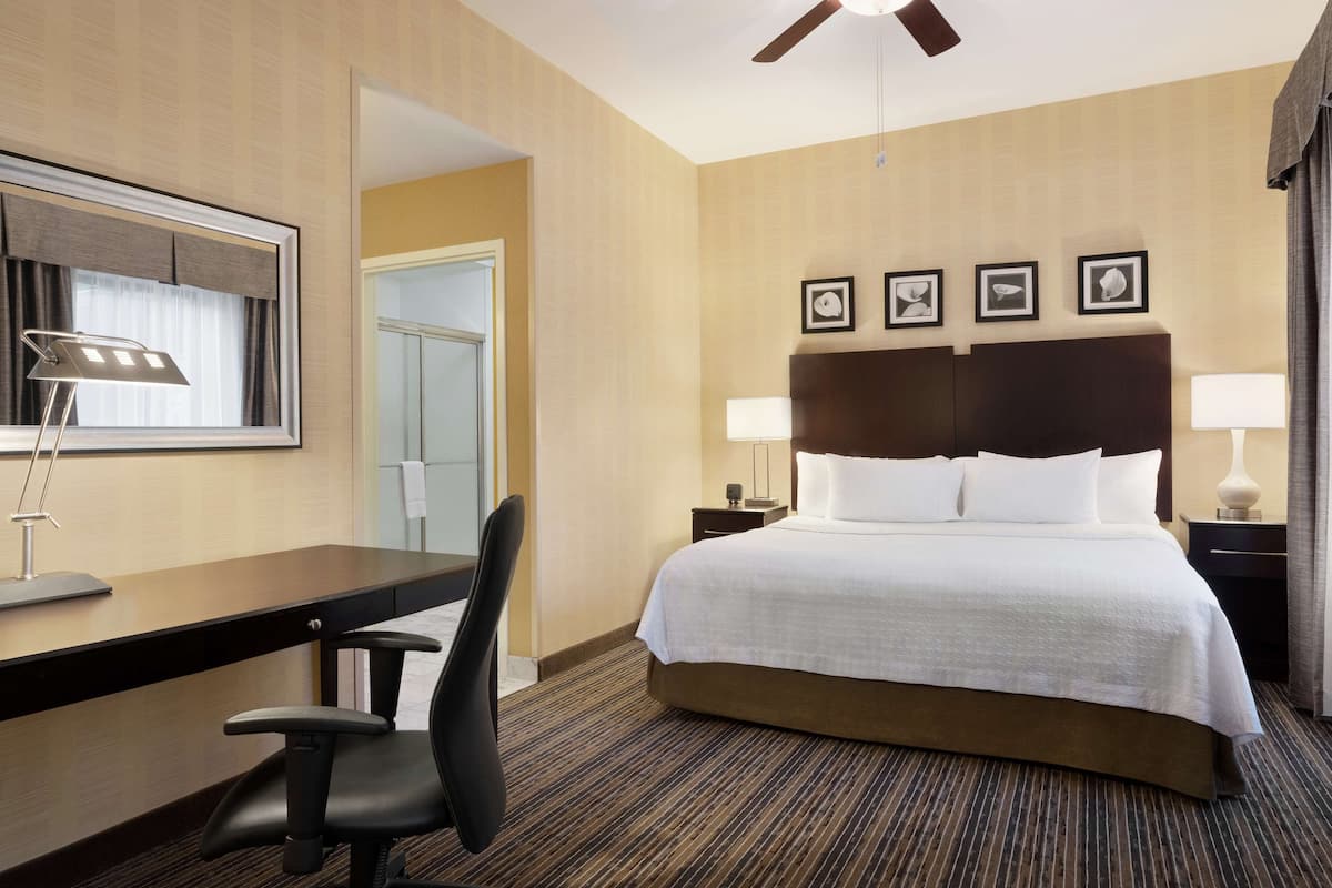 A hotel room with a bed, desk, chair, lamps, and a ceiling fan.