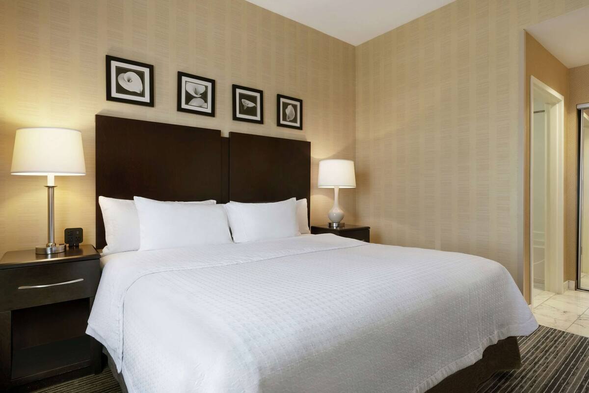 A hotel room with a large bed, two bedside tables with lamps, a dark wood headboard, and framed pictures on the wall.