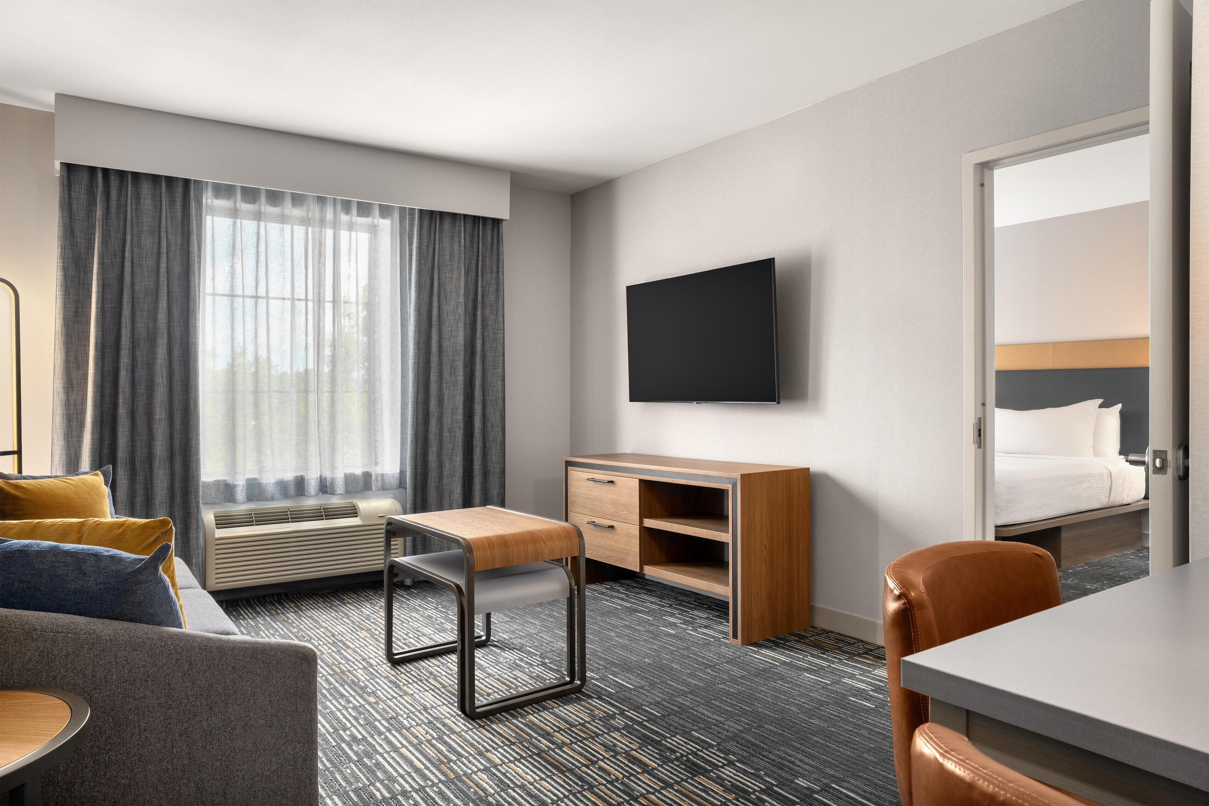 A hotel room with a bed, a desk, a chair, a TV, and a window with curtains.