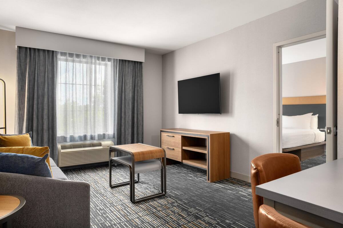 Una habitación de hotel con cama, escritorio, silla, televisor y ventana con cortinas.