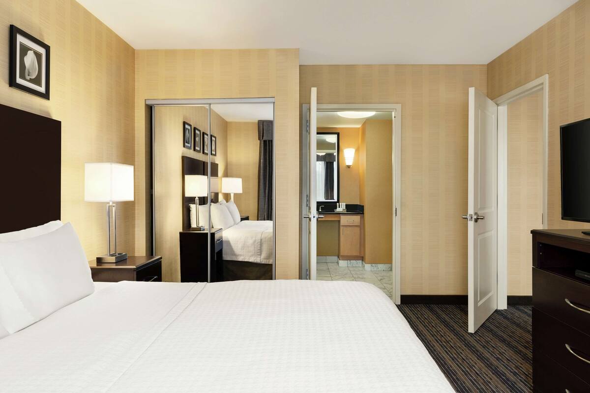 A hotel room with a large bed, a desk with a chair, a television, and a bathroom visible through an open door.