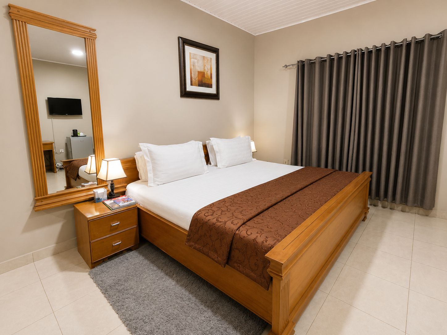Een hotelkamer met een groot bed, een nachtkastje met een lamp, een flatscreen televisie aan de muur en een ingelijst schilderij boven het bed.