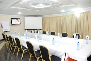 A conference room with a long table, chairs, water bottles, and a projector screen. - Eastgate Hotel (Accra)