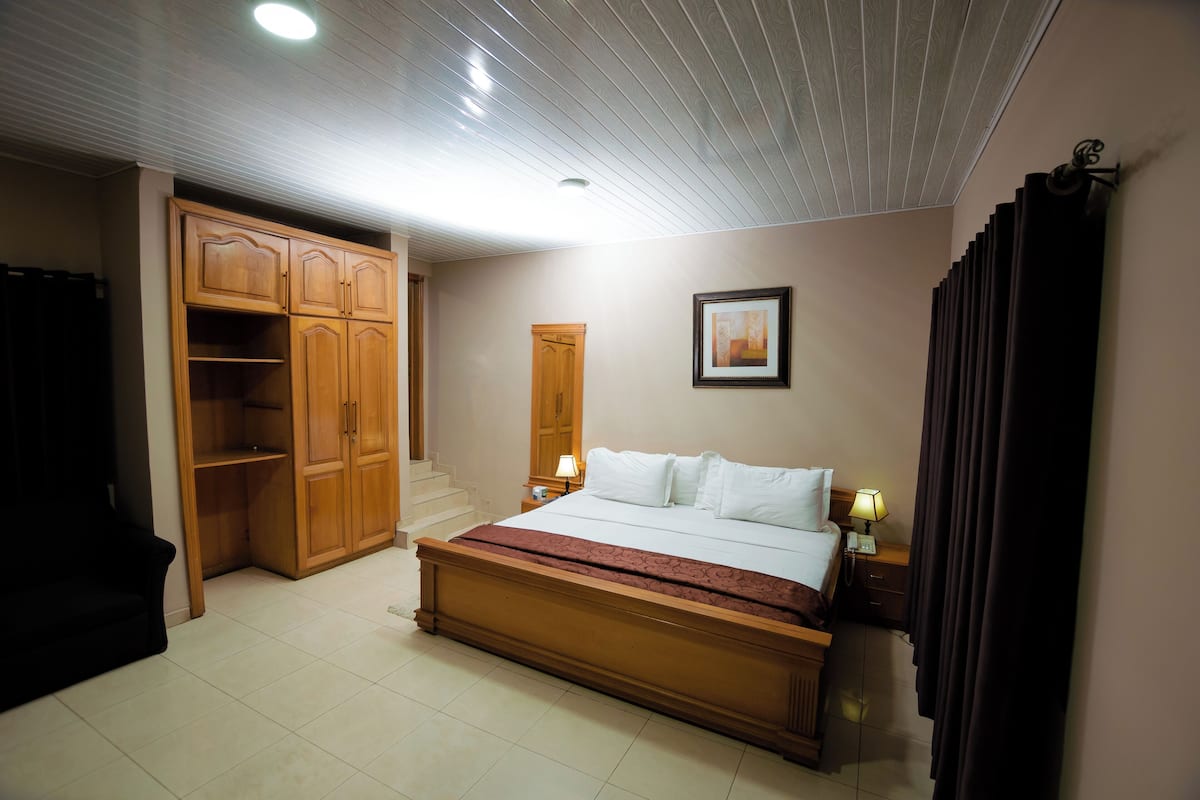 A bedroom with a large bed, wooden wardrobe, and a nightstand with a lamp.