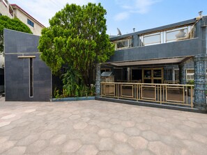 A modern two-story building with a large tree in front, a covered outdoor seating area, and a stone facade. - Eastgate Hotel (Accra)