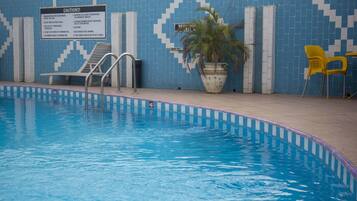 An indoor swimming pool with a sign listing pool rules, a potted plant, and yellow chairs.