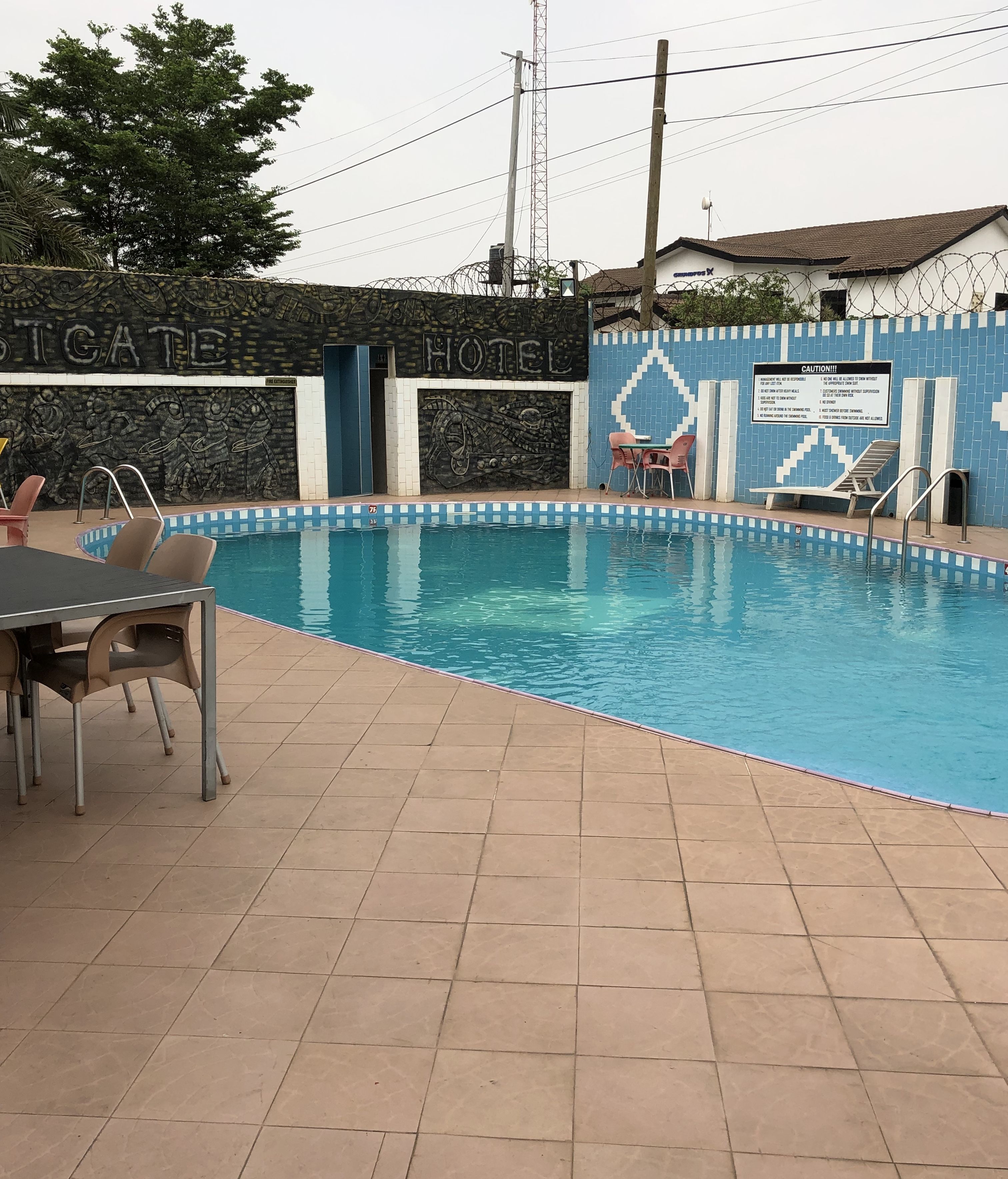 A swimming pool with a tiled deck, lounge chairs, and a wall with a 'Hotel' sign.