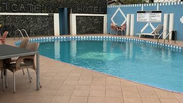 A swimming pool with a tiled deck, lounge chairs, and a wall with a 'Hotel' sign.