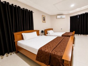 A hotel room with two beds, a nightstand, a lamp, and an air conditioning unit. - Eastgate Hotel (Accra)