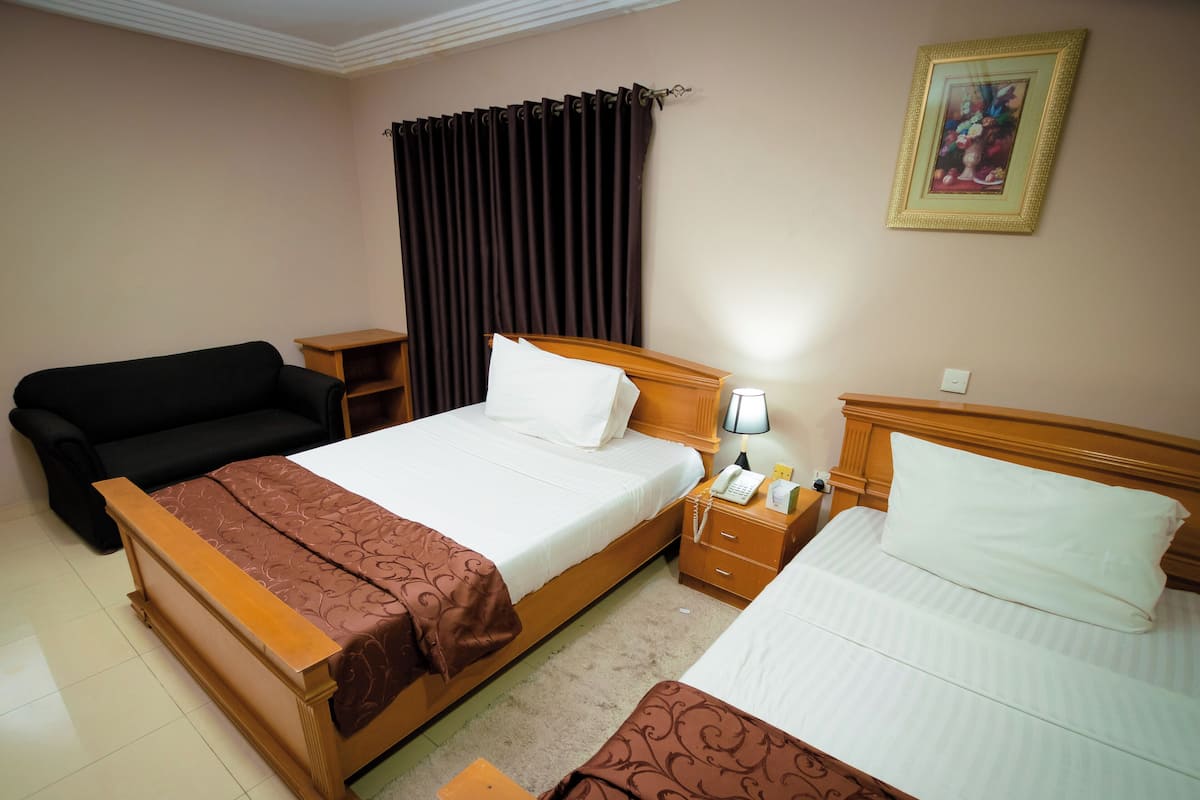 A hotel room with two beds, a sofa, a nightstand with a lamp, and a painting on the wall.