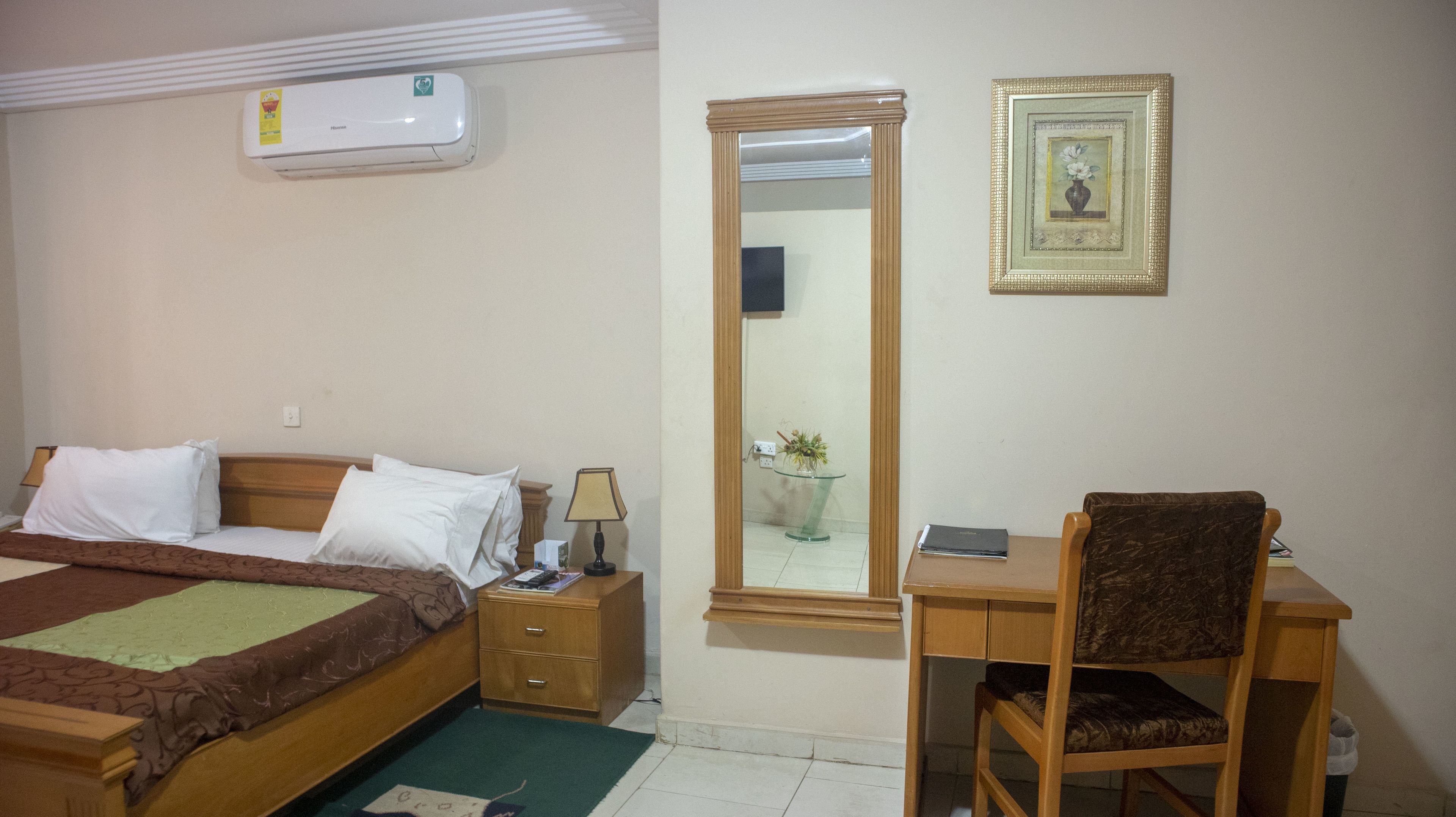 A bedroom with a bed, bedside table, lamp, and a desk with a chair.