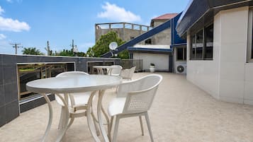 Une terrasse extérieure avec une table ronde et des chaises, une antenne parabolique et, au fond, un bâtiment avec un toit rouge.