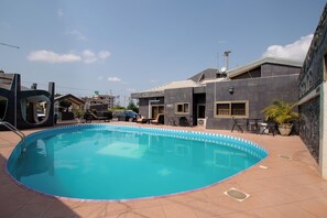 A swimming pool with a tiled deck, surrounded by buildings and a clear sky. - Eastgate Hotel (Accra)