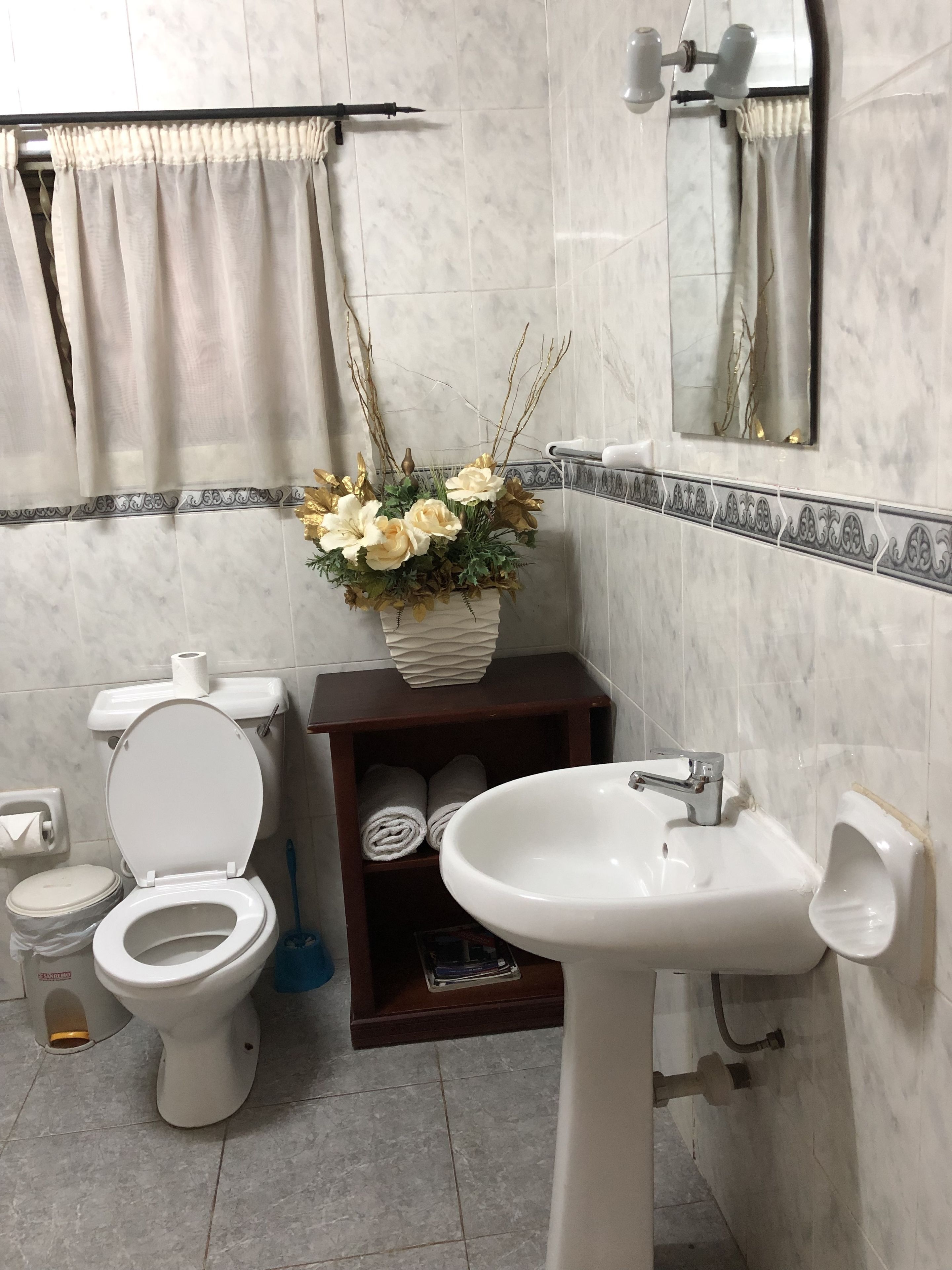A bathroom with a toilet, sink, and a decorative vase with flowers.