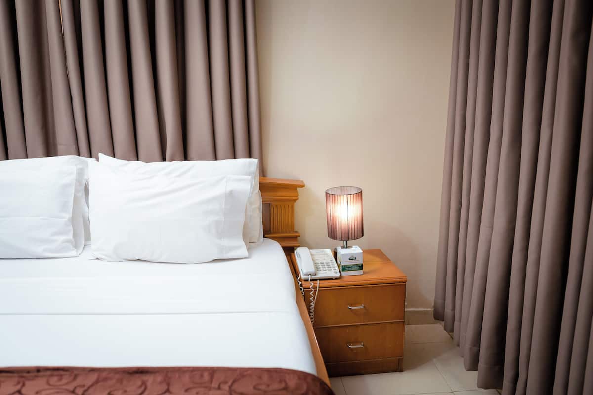 A neatly made bed with white linens and pillows, a bedside lamp, a telephone, and a wooden nightstand.