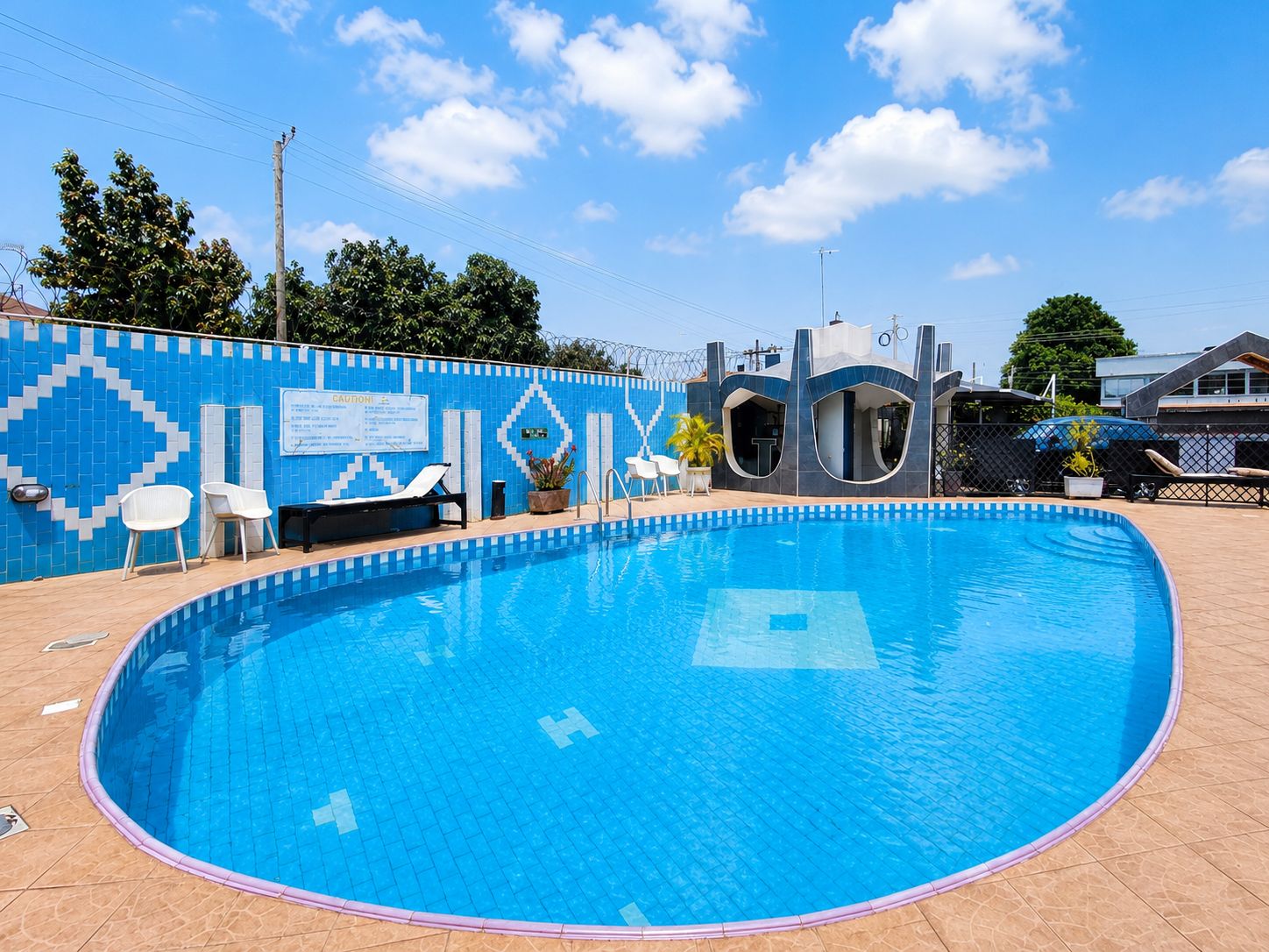 Une piscine bordée de carreaux bleus, avec des chaises longues et un mur aux motifs bleus et blancs.