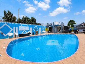A swimming pool with a blue tiled border, lounge chairs, and a blue and white patterned wall. - Eastgate Hotel (Accra)
