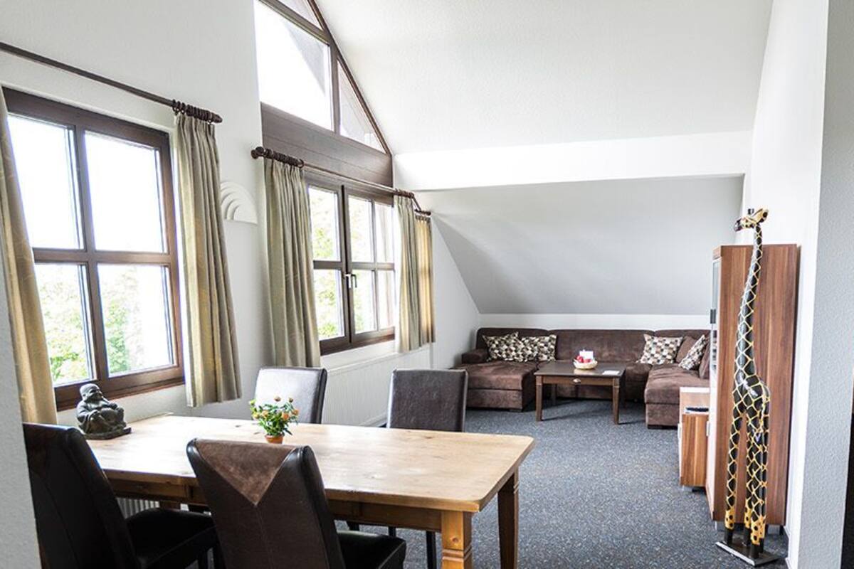 Una habitación con una mesa de comedor, sillas, un sofá y una ventana con cortinas.
