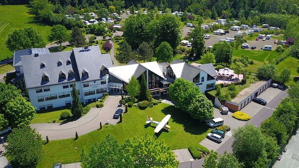 Luchtbeeld van een hotel met een groot gebouw, een parkeerplaats en een klein vliegtuig op het gazon.