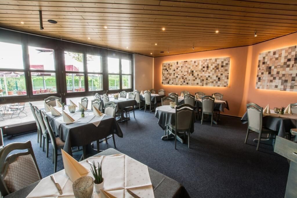 A restaurant with multiple tables and chairs, large windows, and a wooden ceiling.