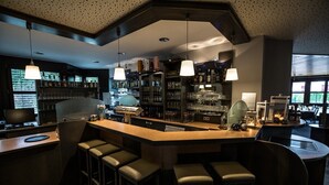 Een bar met een gebogen toonbank, meerdere krukken en hangende hanglampen.