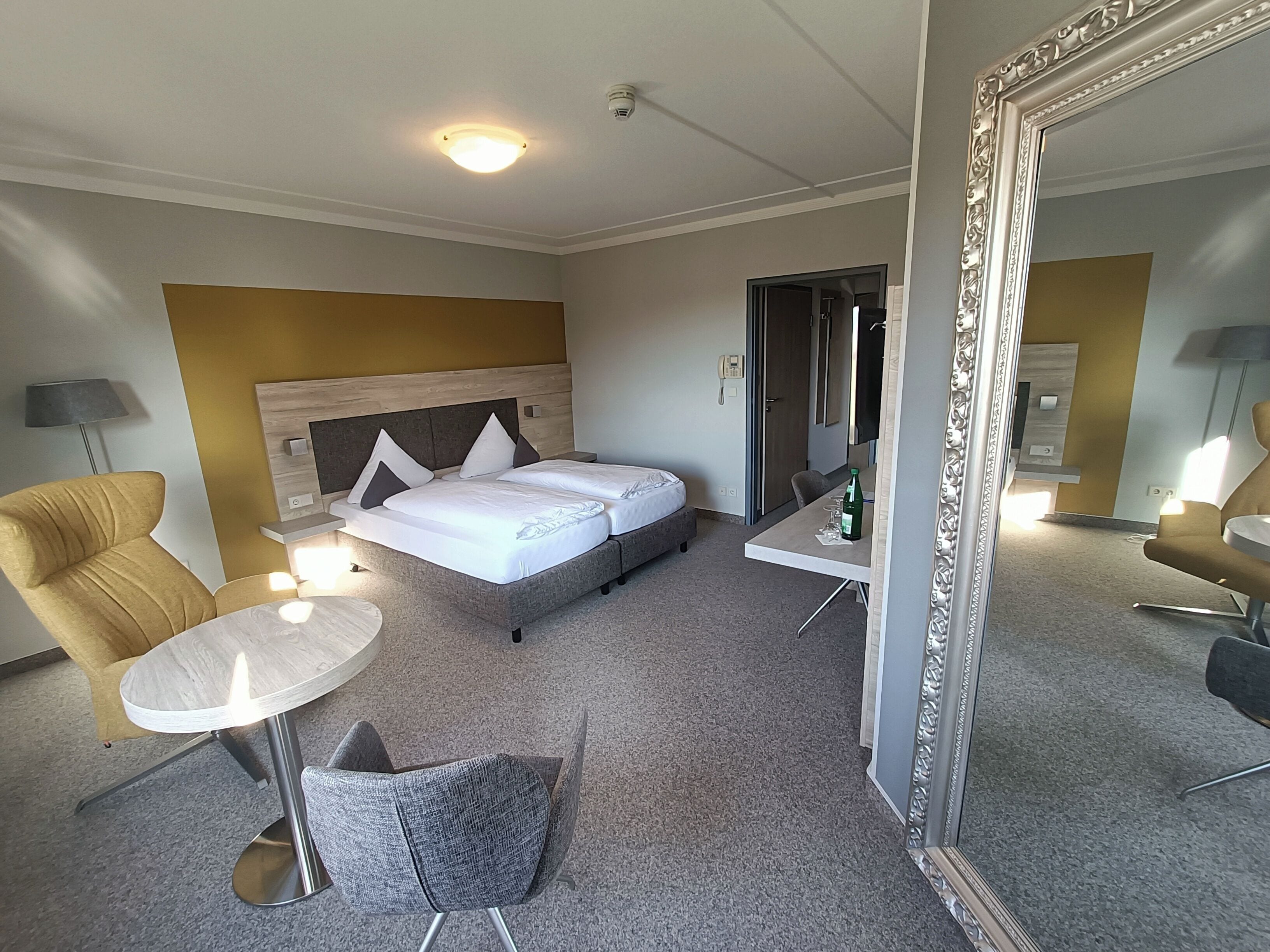 Una habitación de hotel con cama, escritorio, silla, mesita y espejo.