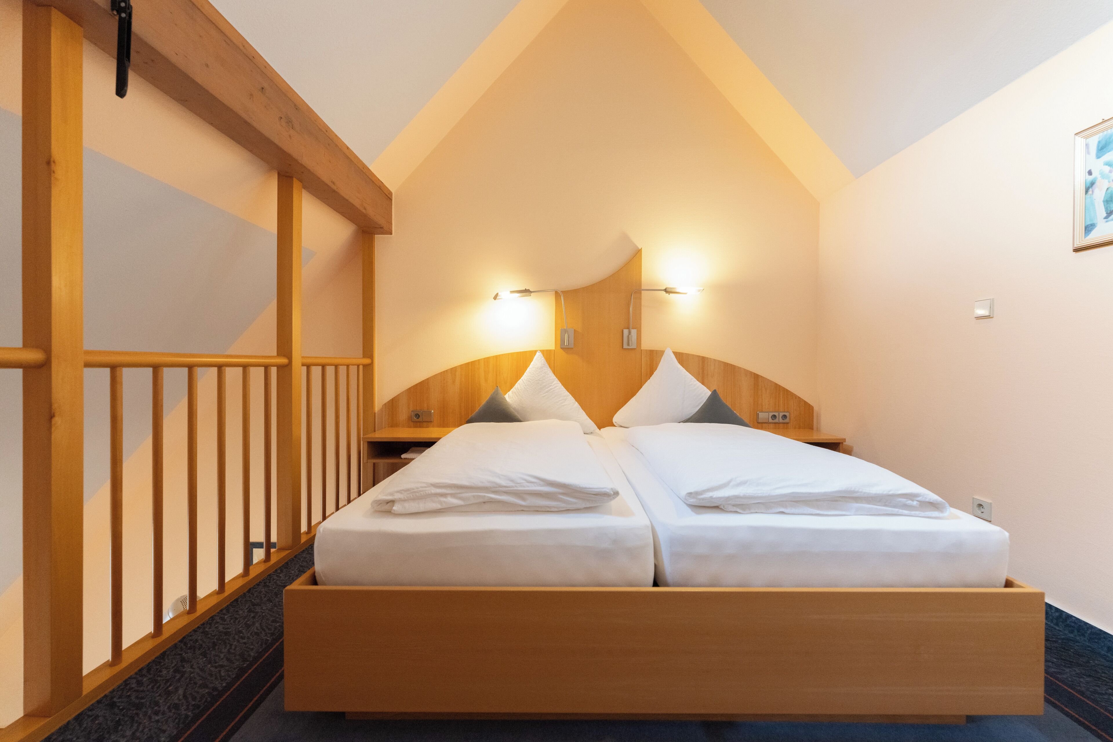 A double bed with two pillows, a wooden headboard, and a nightstand with a lamp.