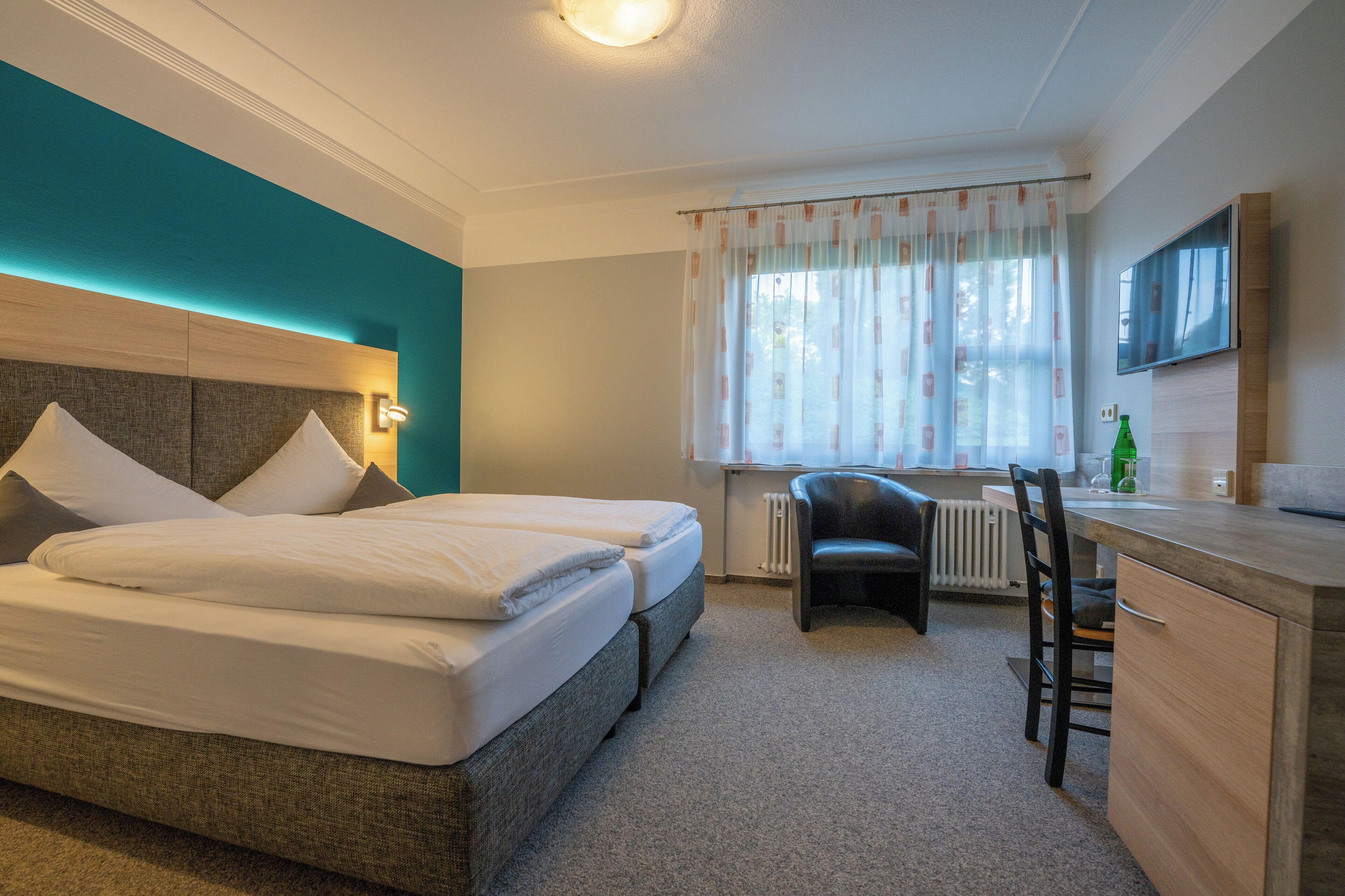 A hotel room with two beds, a desk, a chair, and a TV.