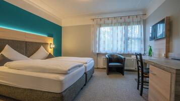 A hotel room with two beds, a desk, a chair, and a TV.
