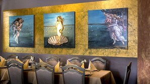 Een restaurant met een lange tafel gedekt voor een maaltijd, met een decoratieve muur met daaraan drie schilderijen.
