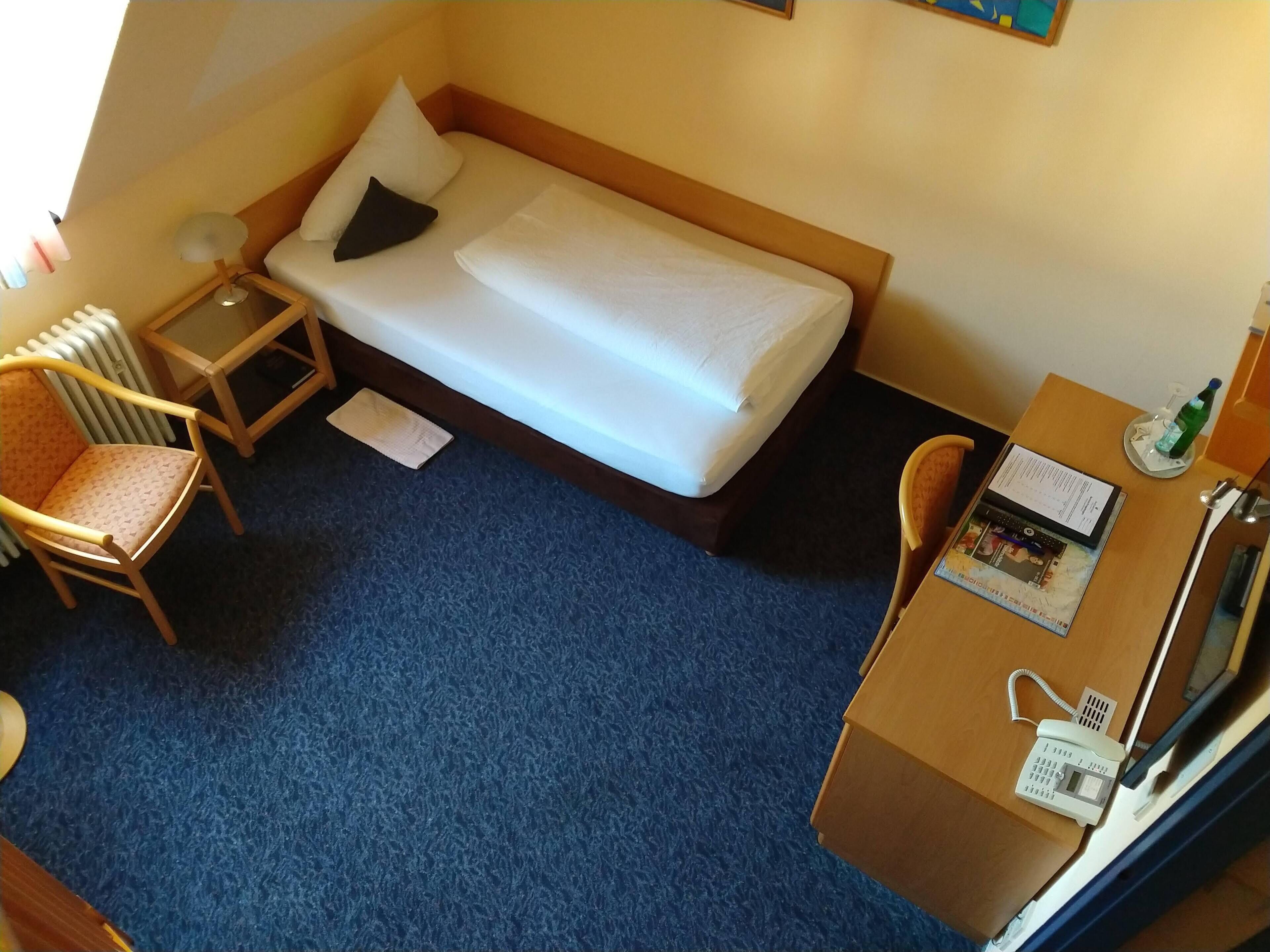 A hotel room with a single bed, a desk with a telephone, a chair, and a radiator.
