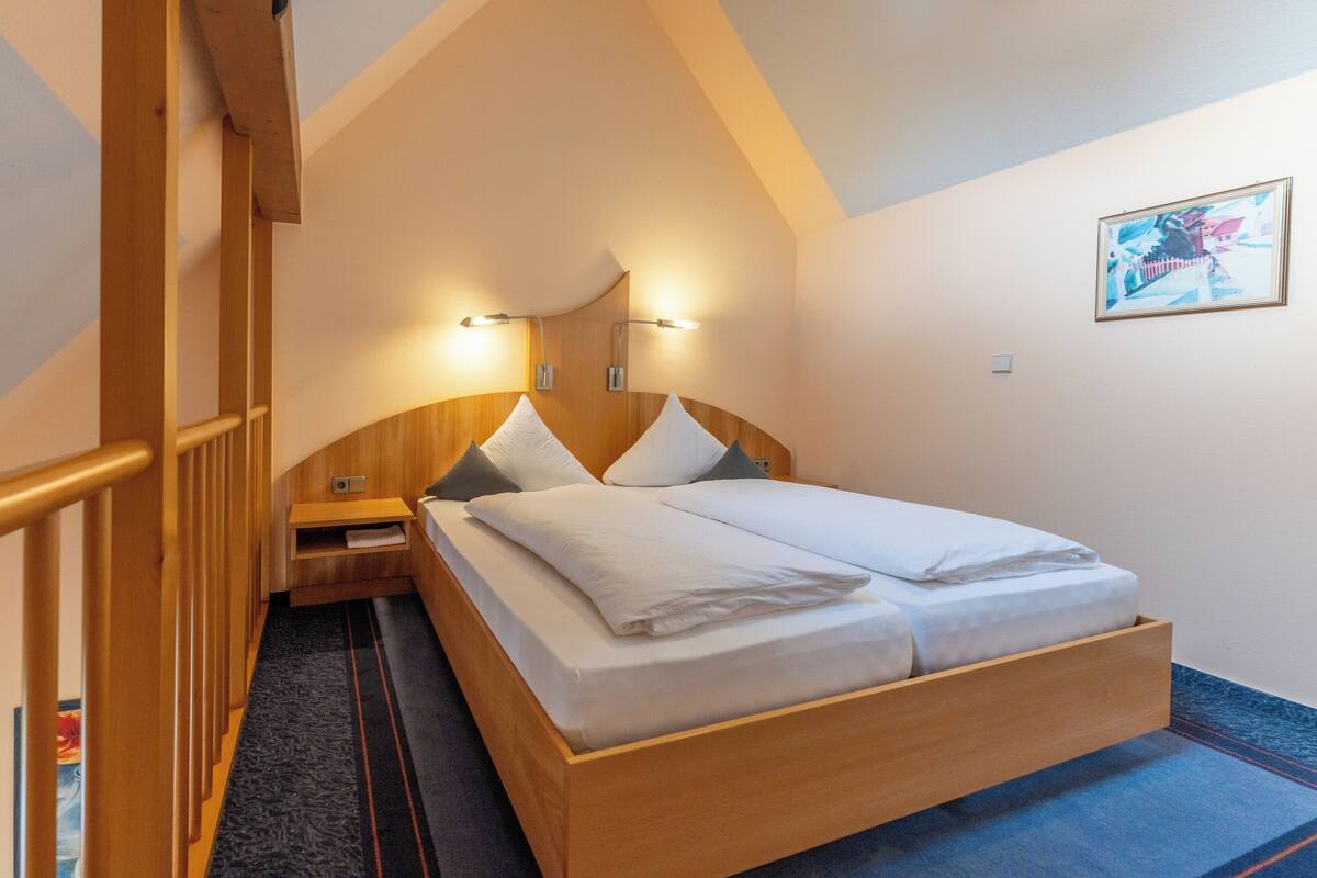 Un dormitorio con una cama de madera, una mesita de noche y una lámpara fijada a la pared.