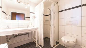 Un baño con lavamanos blanco, espejo e inodoro. Hay una cortina de ducha y piso de baldosas.