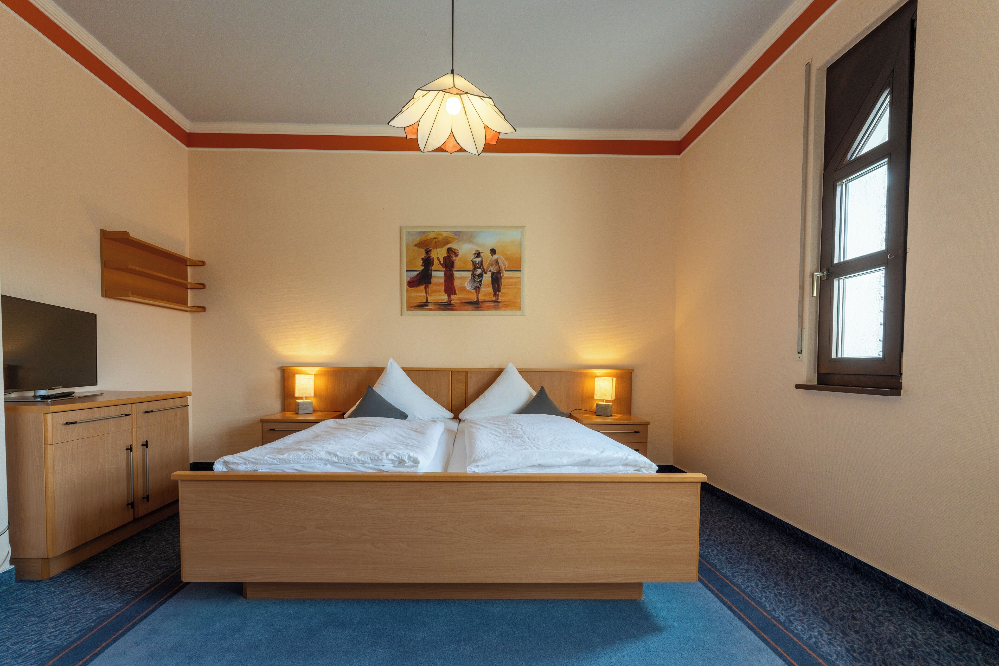Habitación de hotel con cama de madera, lámparas de noche, un cuadro en la pared y televisor sobre un mueble.