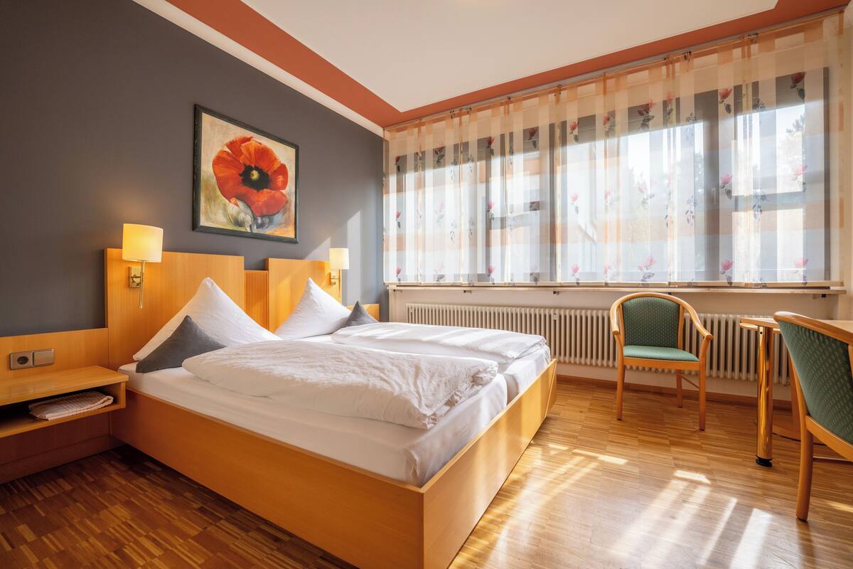 Una habitación de hotel con una cama de madera, dos mesitas de noche, una silla y una ventana con cortinas.