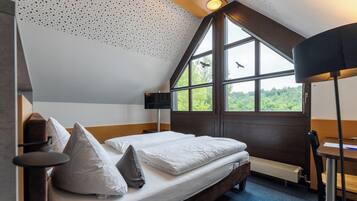 A bedroom with a large window, a bed with pillows, a desk, and a chair.