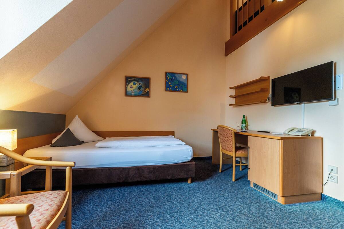 Habitación de hotel con cama, escritorio, silla y televisor.