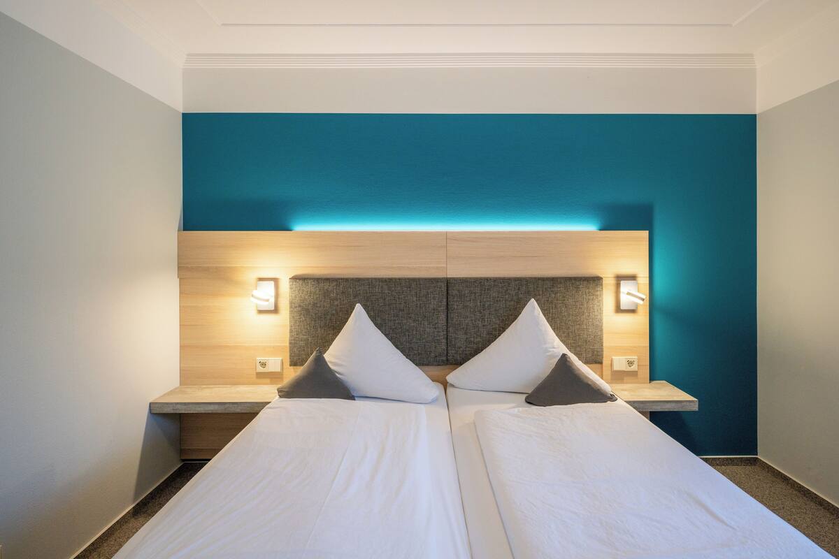 Una cama doble con cabecera de madera y dos mesitas de noche, cada una con una lámpara.