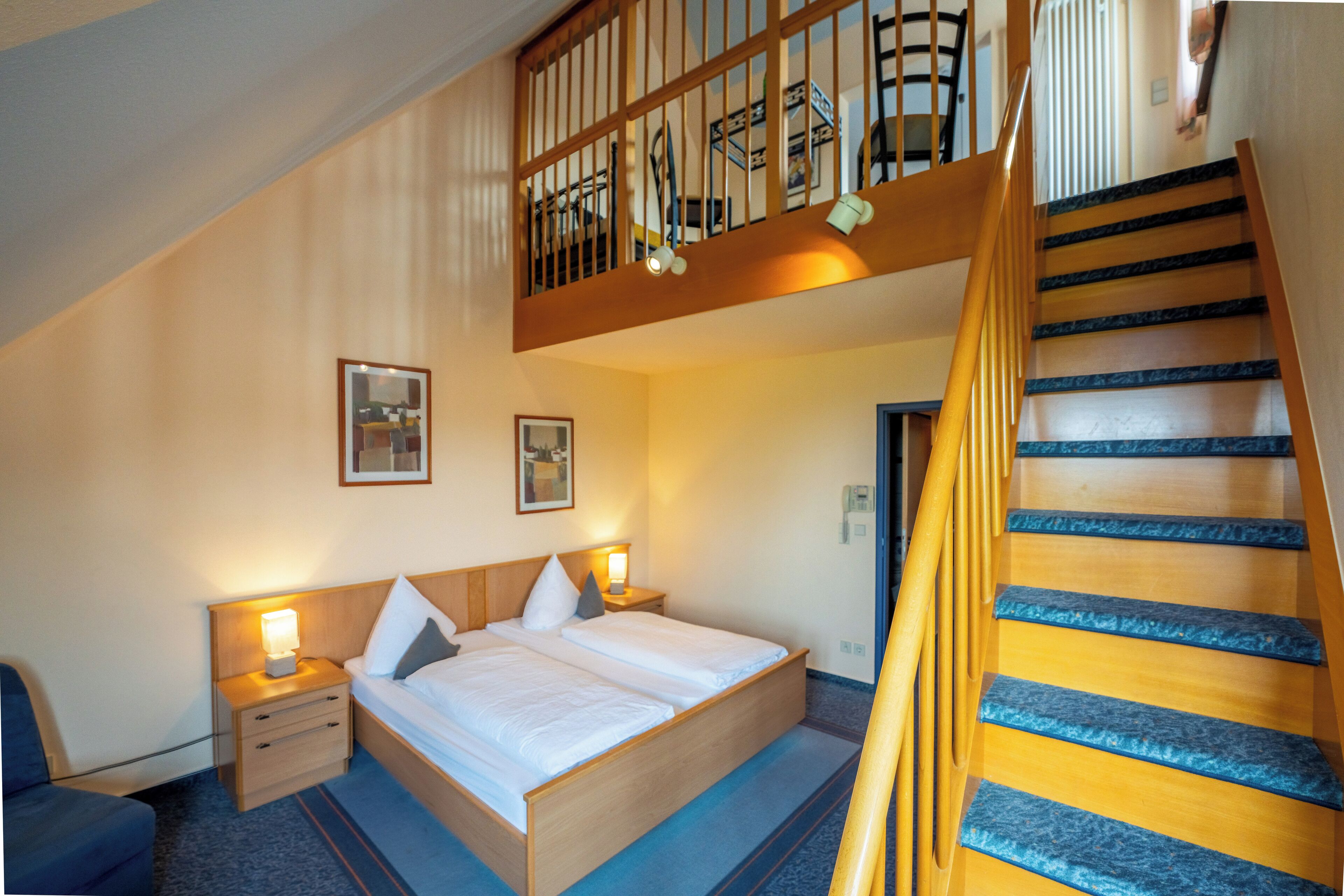 A bedroom with a wooden bed, a nightstand, a desk, and a staircase.