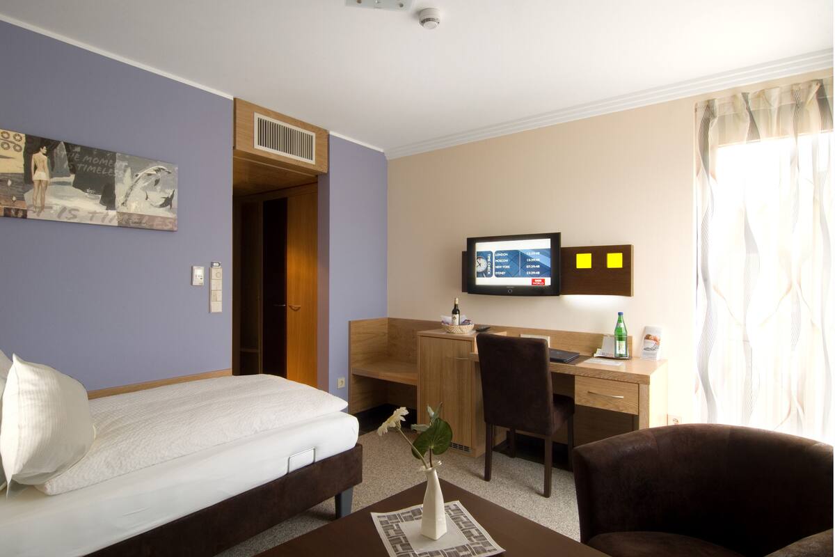 Habitación de hotel con cama, escritorio, silla y televisor en la pared.