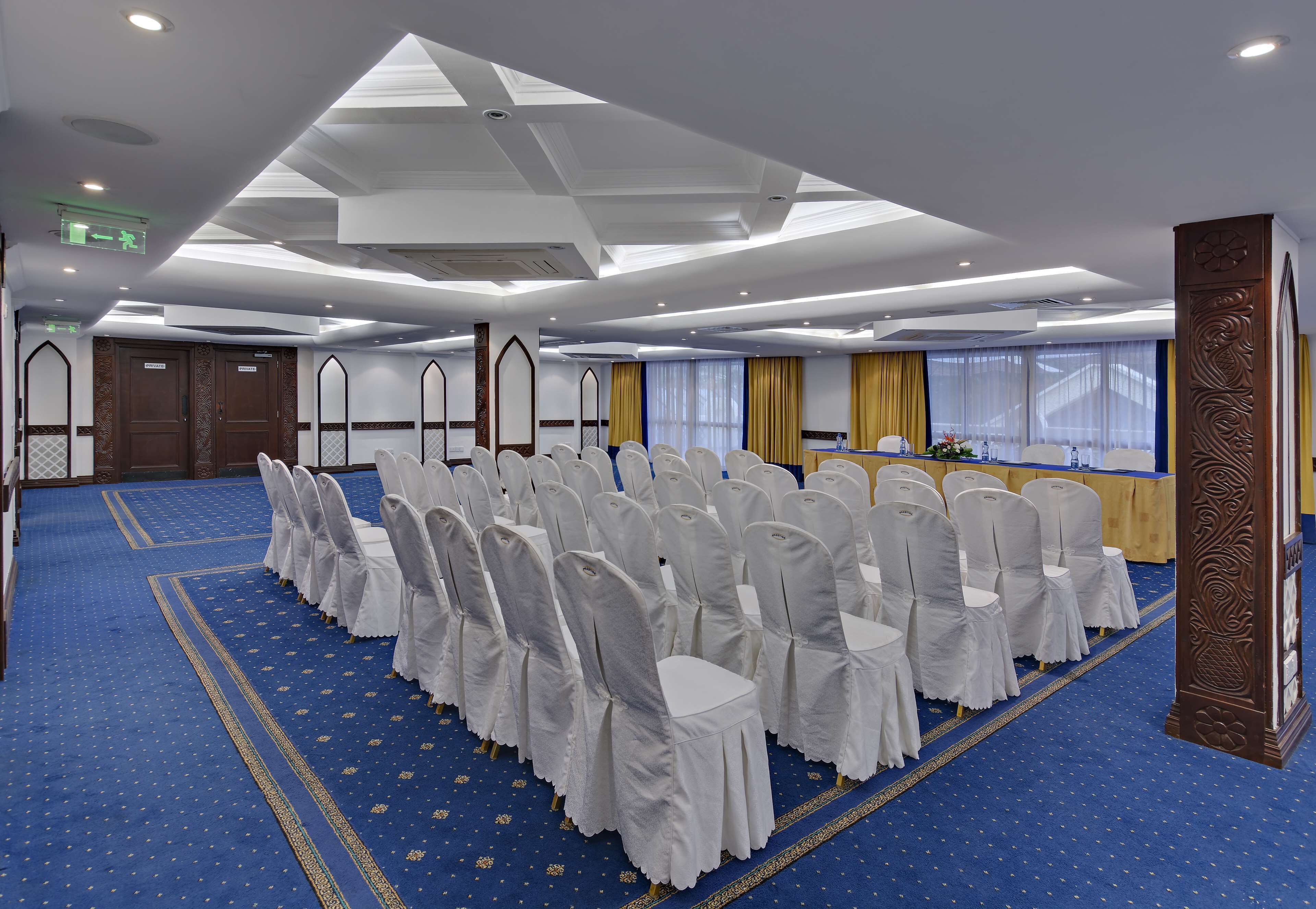 A conference room with rows of white chairs, a podium, and a blue carpet.