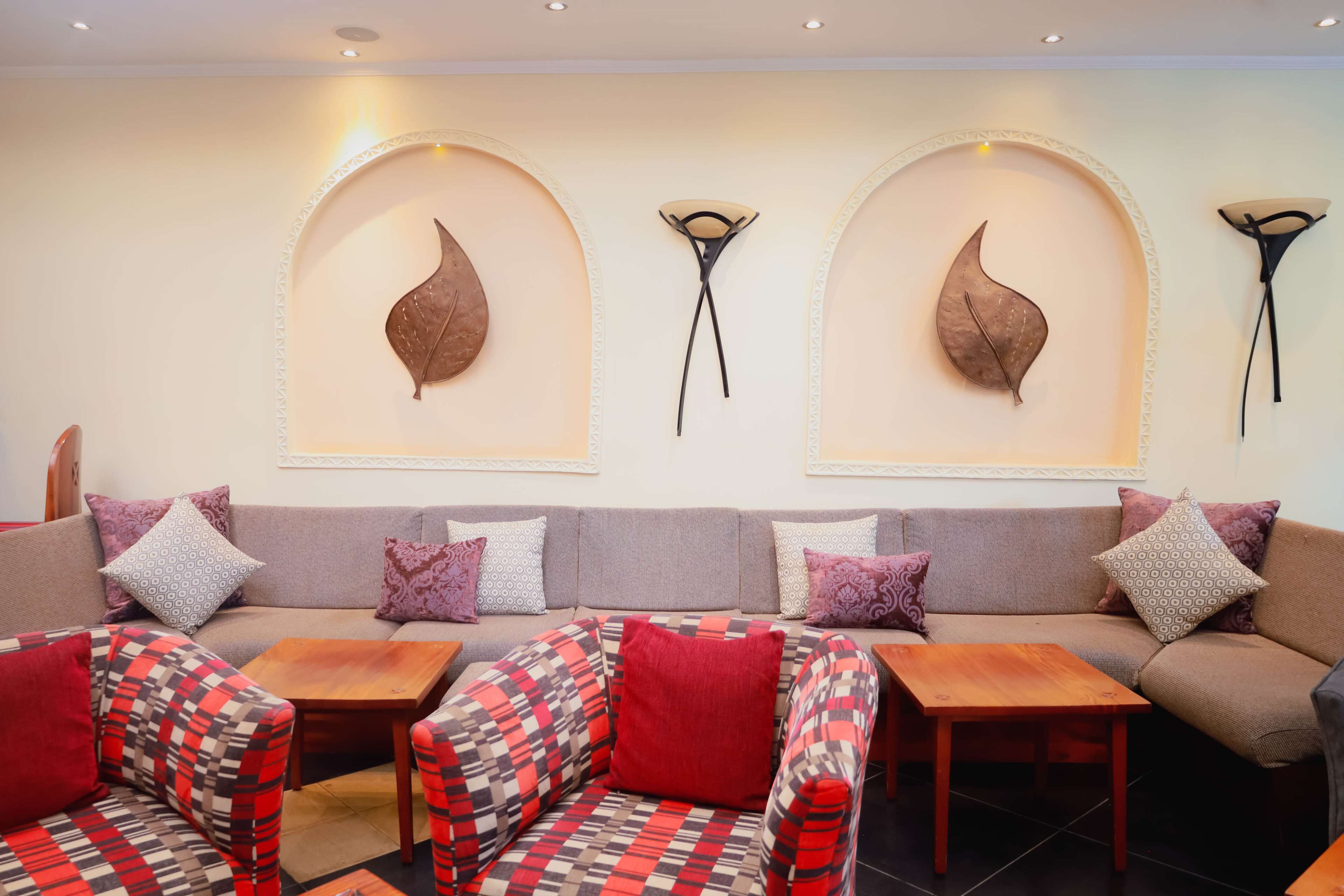 A modern lounge area with a sofa set, two wooden tables, and patterned armchairs.