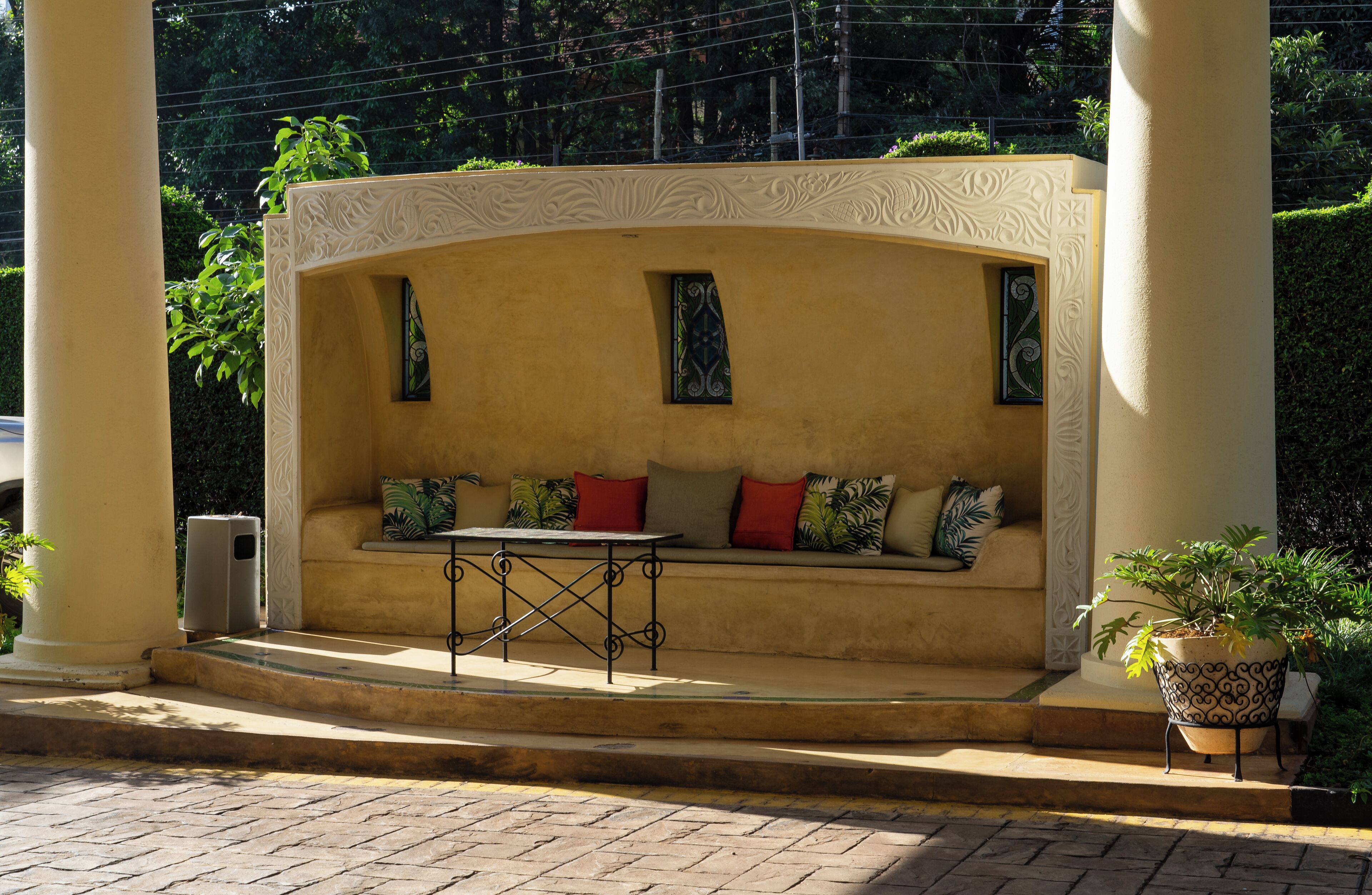 A sunlit outdoor seating area with a curved bench, a small table, and decorative columns.