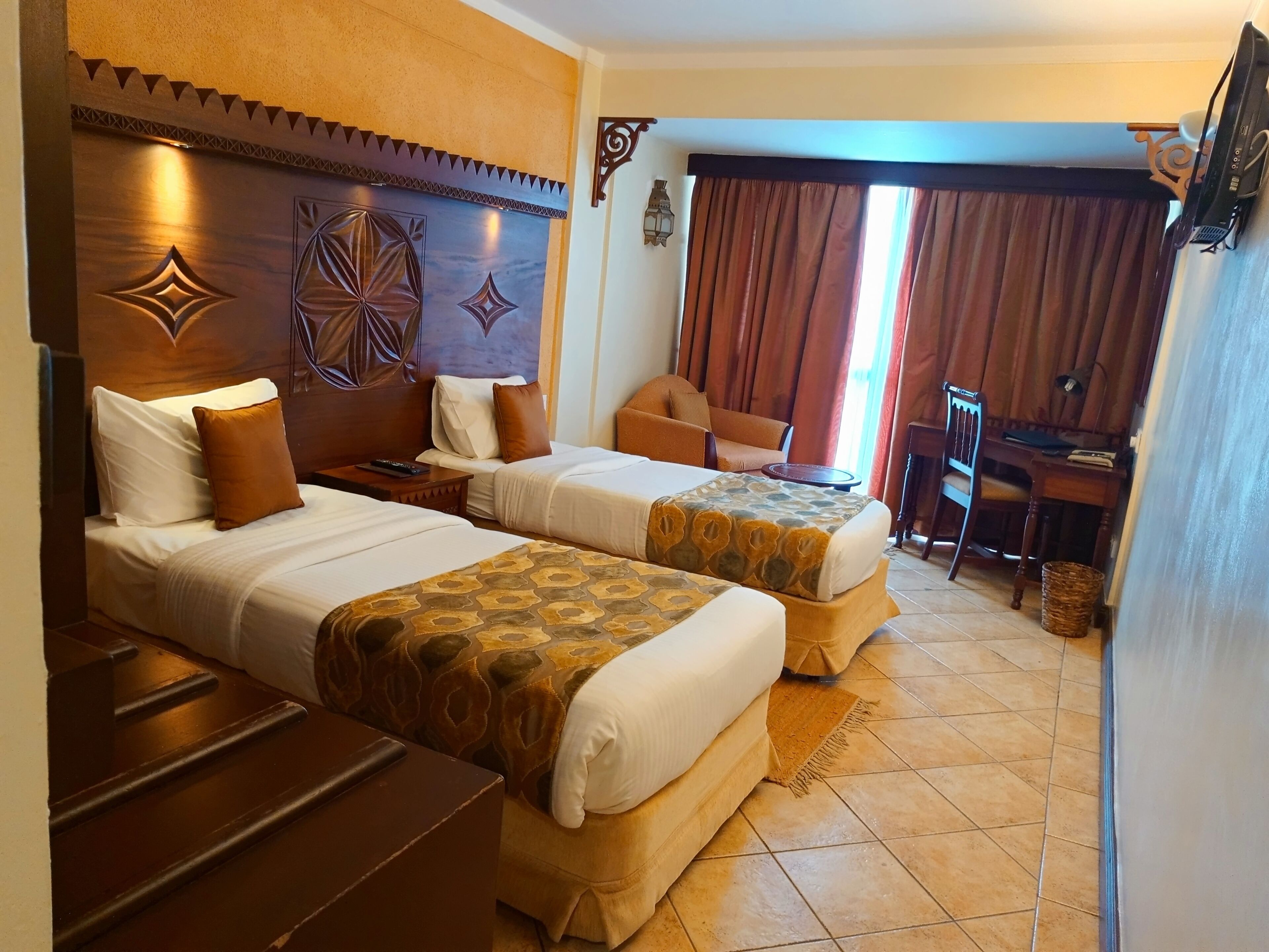 A hotel room with two beds, a desk, a chair, and a TV.