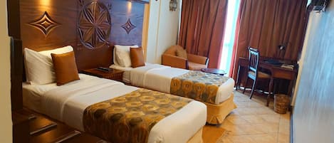 A hotel room with two beds, a desk, a chair, and a TV.