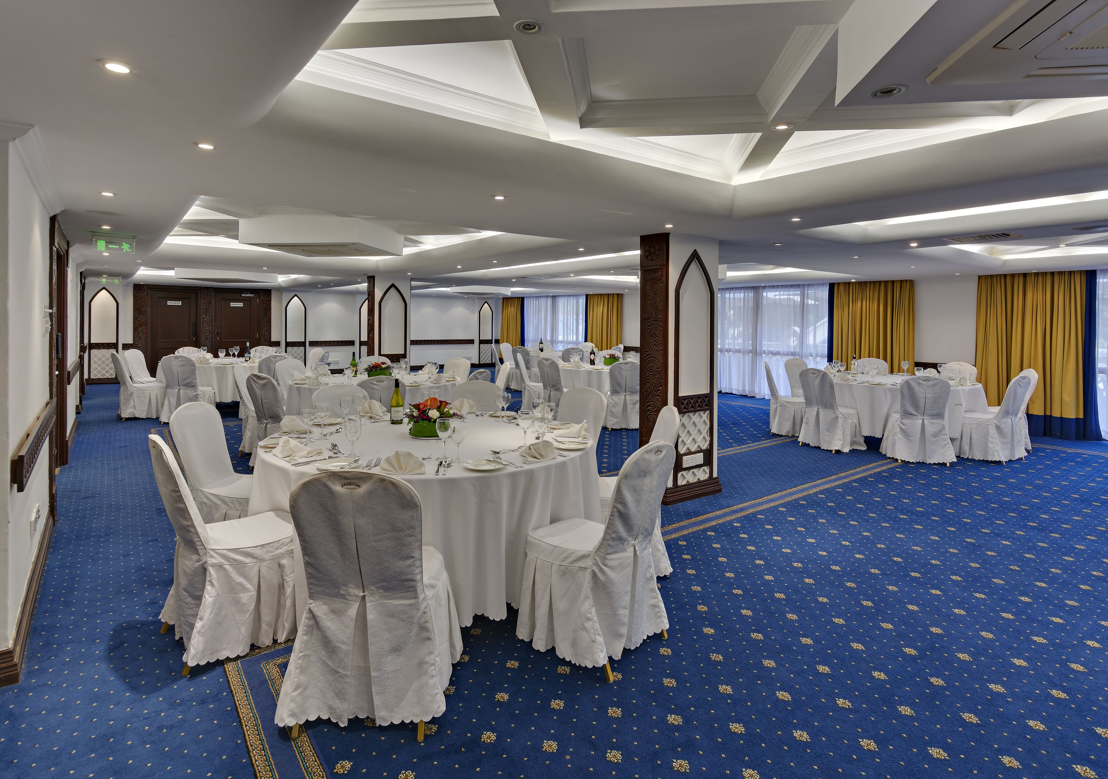 A banquet hall with round tables, white chairs, and a blue carpet.