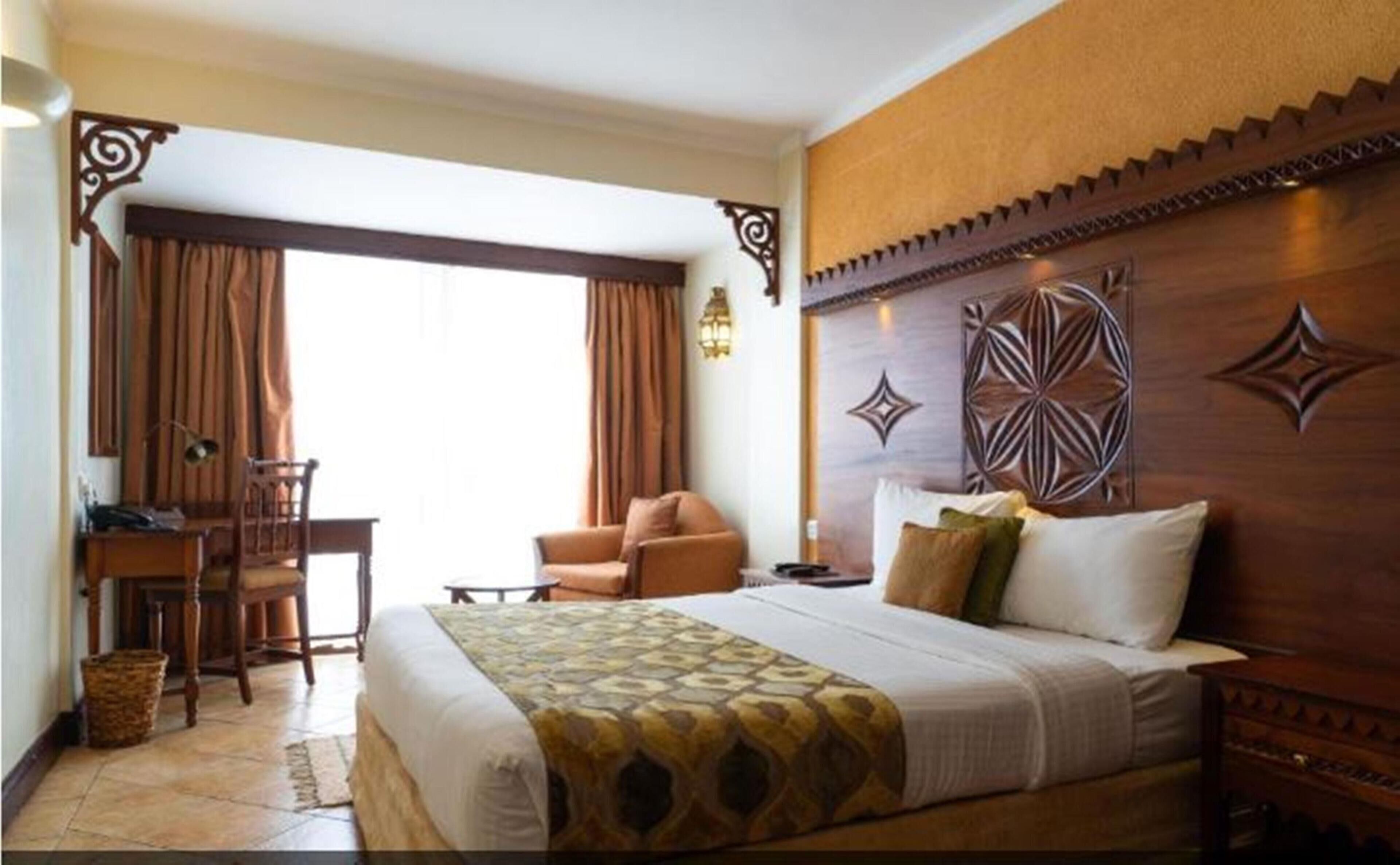 Una habitación de hotel con cama, escritorio, silla y ventana con cortinas.