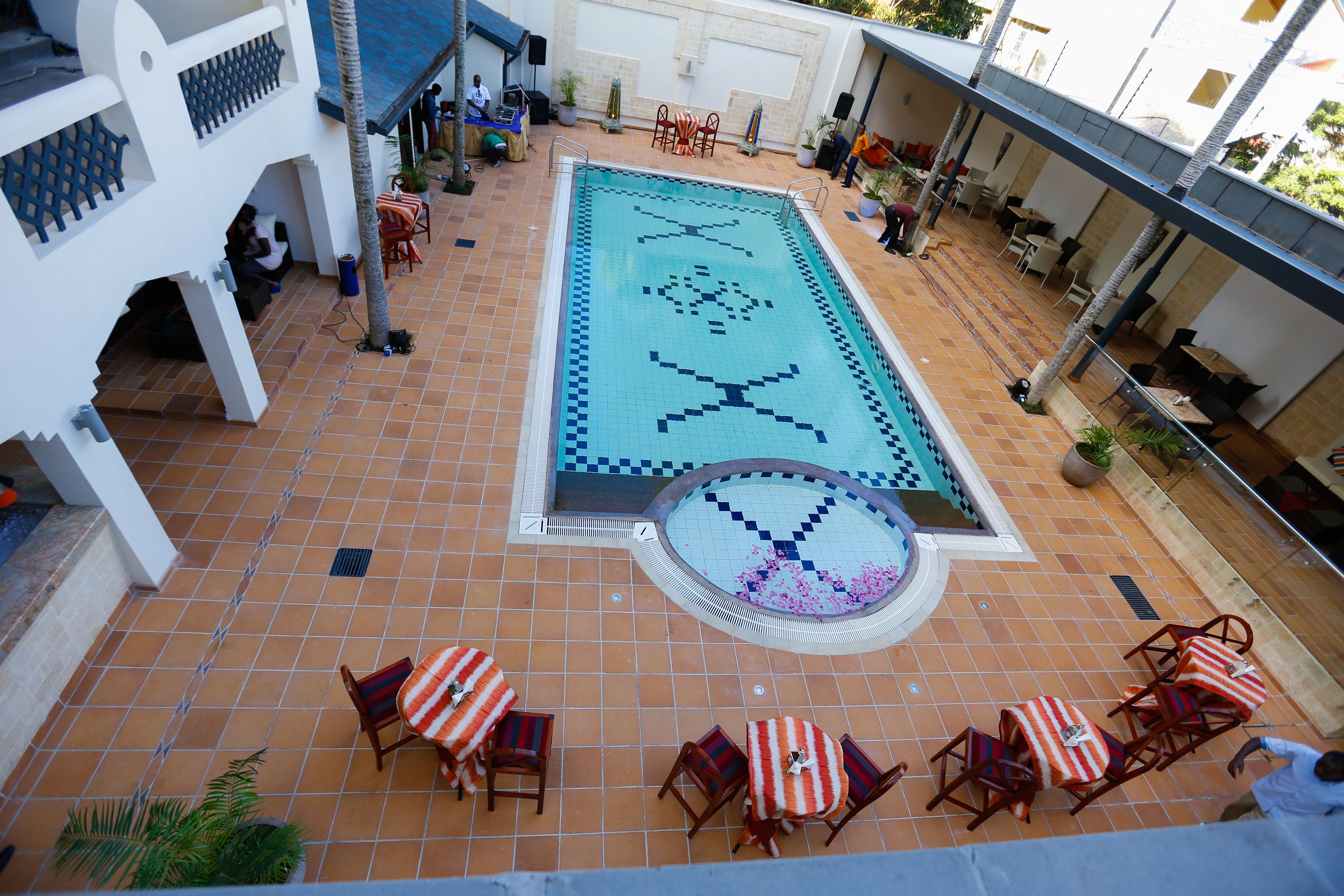 A rooftop pool area with tiled flooring, a central pool, and surrounding lounge chairs and tables.