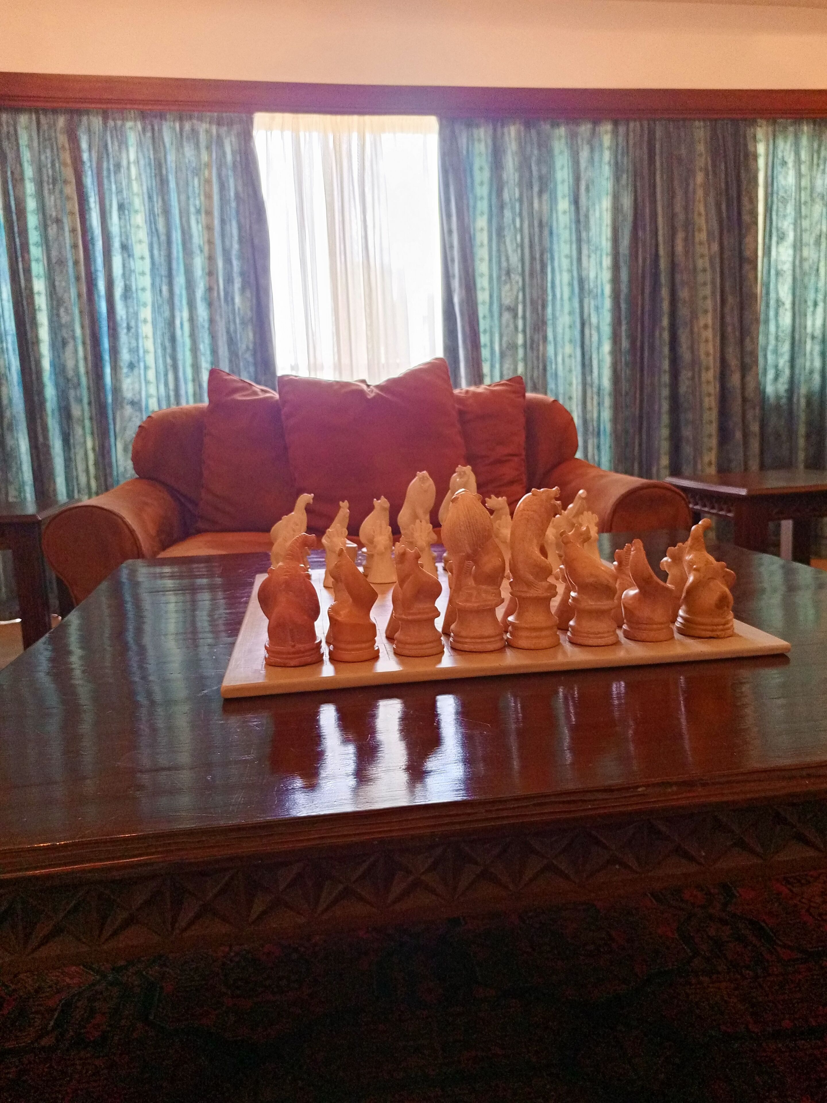 A chessboard on a wooden table with a sofa and curtains in the background.